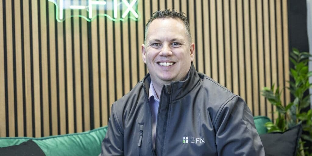 Craig Atkins, Managing Director of 1-Fix is sat on a sofa with the business logo illuminated behind him.
