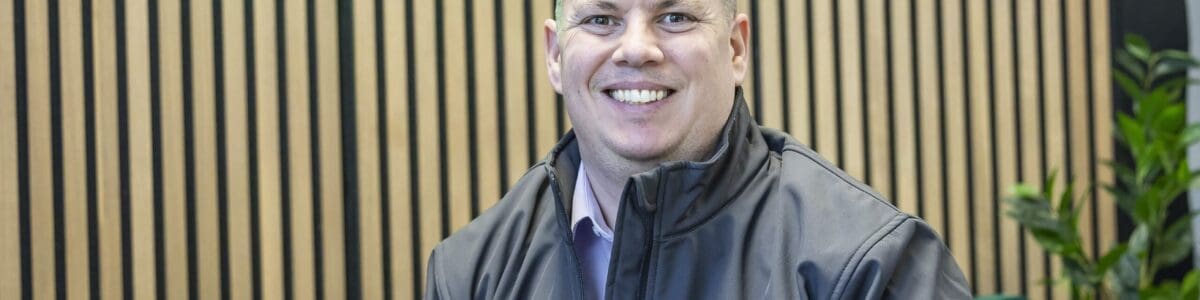 Craig Atkins, Managing Director of 1-Fix is sat on a sofa with the business logo illuminated behind him.